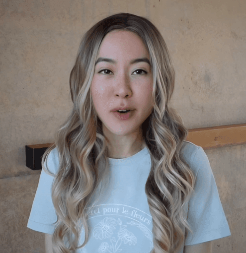 AI-generated avatar of a woman with long wavy blonde hair wearing a light blue shirt, posing against a neutral indoor background.